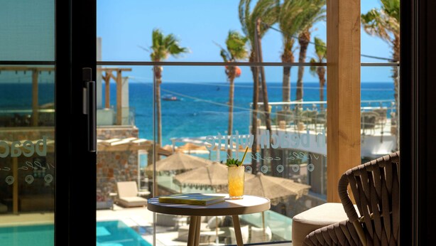 A balcony with a view of the ocean, a glass table with a drink, and a chair. - High Beach White (Hersonissos)
