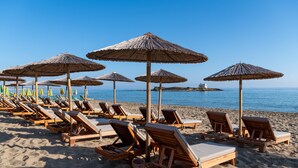 A beach with wooden lounge chairs and thatched umbrellas. - High Beach White (Hersonissos)