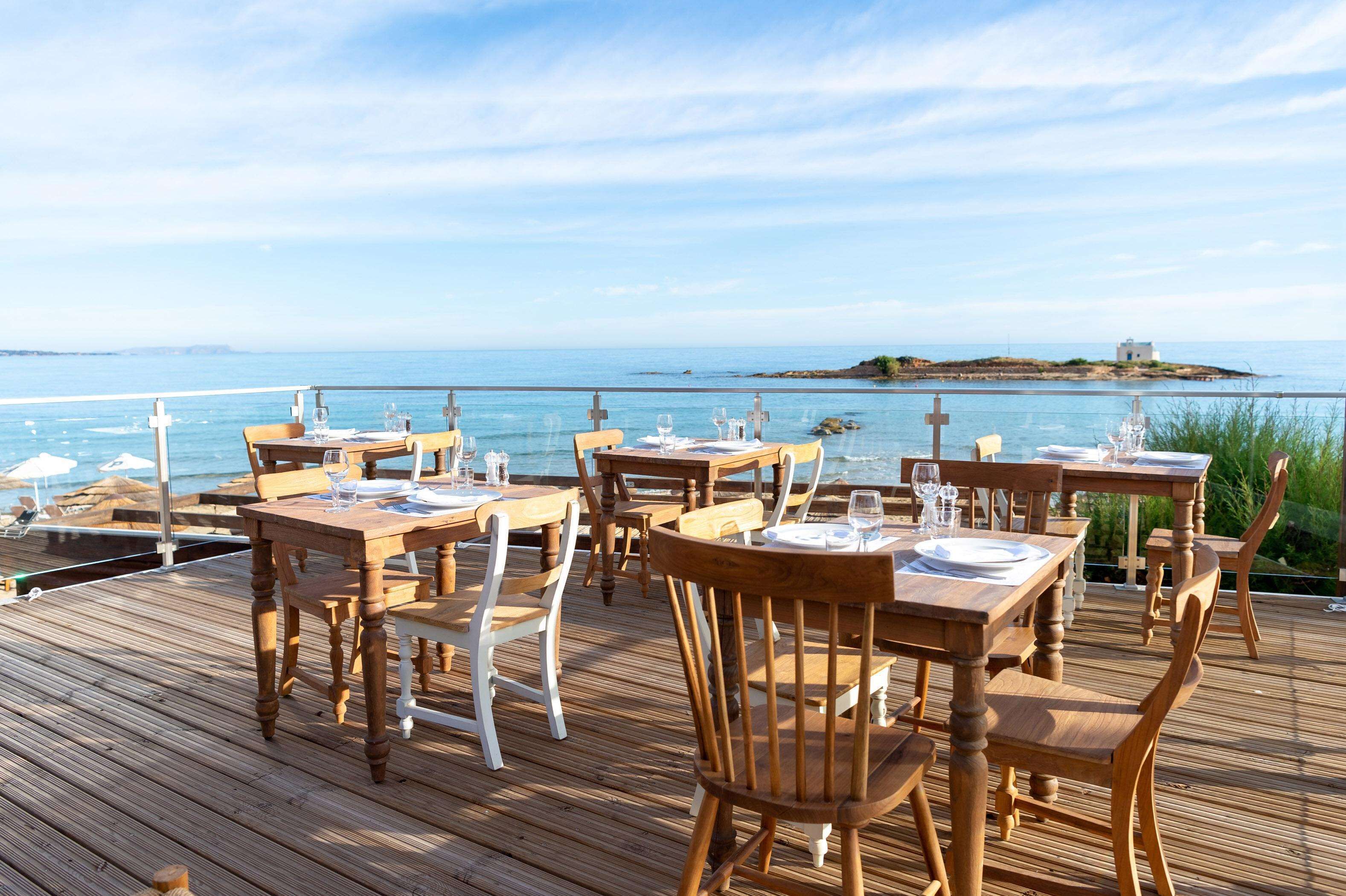 A wooden deck with tables and chairs, overlooking a body of water with a small island in the distance.