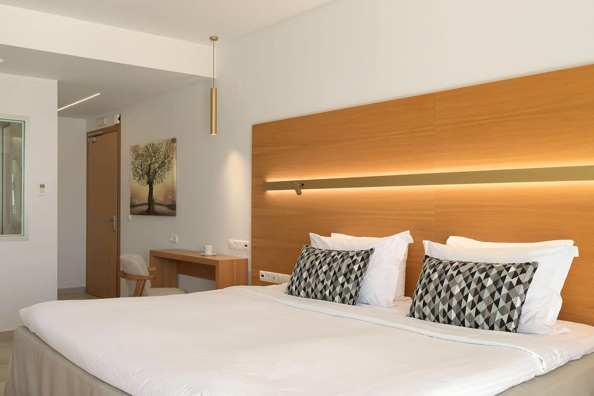 A modern hotel room with a large bed, a desk, a chair, and a glass shower enclosure.