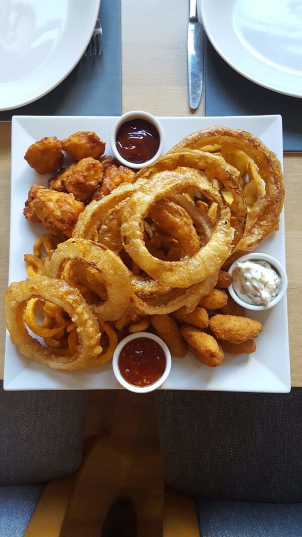 Un plato de cebollas a la romana y nuggets de pollo, acompañado de salsas para mojar.
