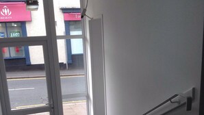 Ingresso di un hotel con una porta in vetro che dà sull'esterno, una ringhiera a destra e vista sulla strada.