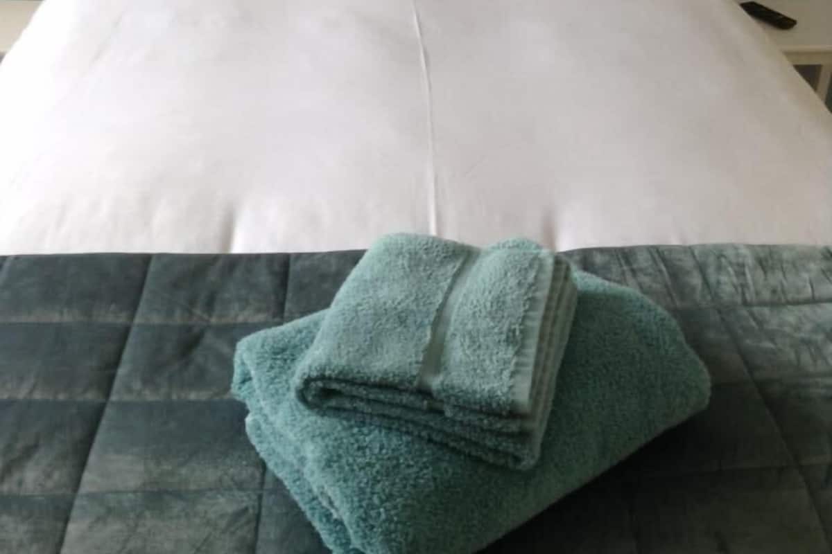 A neatly made bed with white linens and a folded teal towel on a dark-colored bedspread.