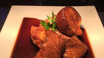 Un plato blanco cuadrado con un trozo de carne y una guarnición sobre un fondo oscuro.
