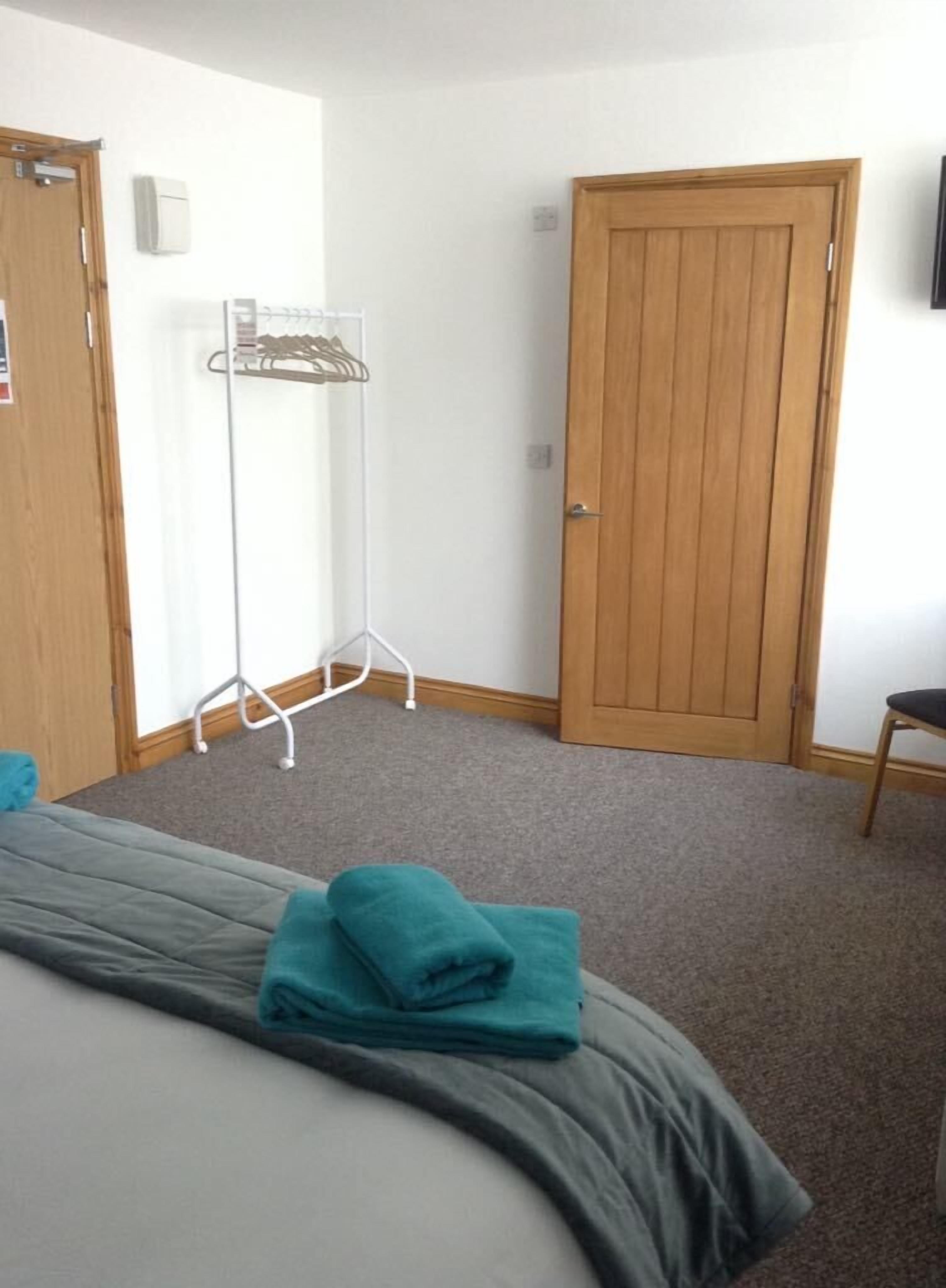 Une chambre d’hôtel avec un lit, une porte en bois, un mur blanc et un radiateur blanc.