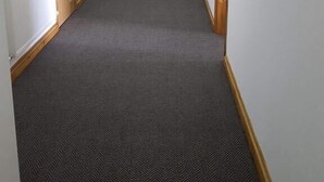 Un corridoio con pavimento rivestito di moquette, pareti bianche, porte in legno e un estintore.