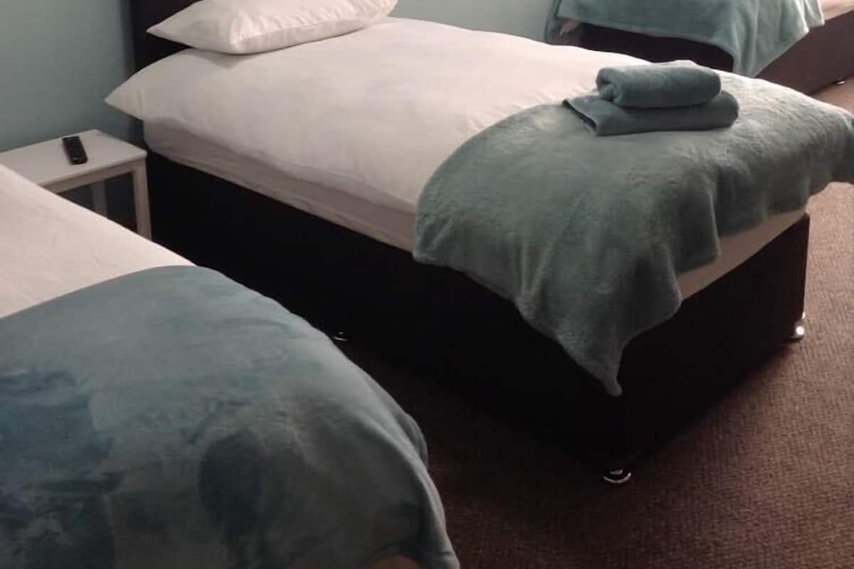A hotel room with two single beds, a nightstand with a remote control, and a wall-mounted lamp.