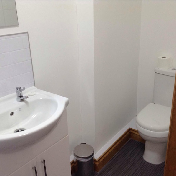 A small bathroom with a white sink, toilet, and a trash can. - The Bear on the Square (Millom)