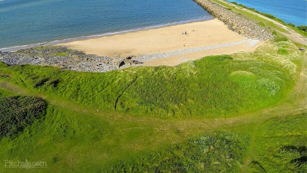 Vista aerea di una zona costiera con spiaggia sabbiosa, costa rocciosa e vegetazione verde.