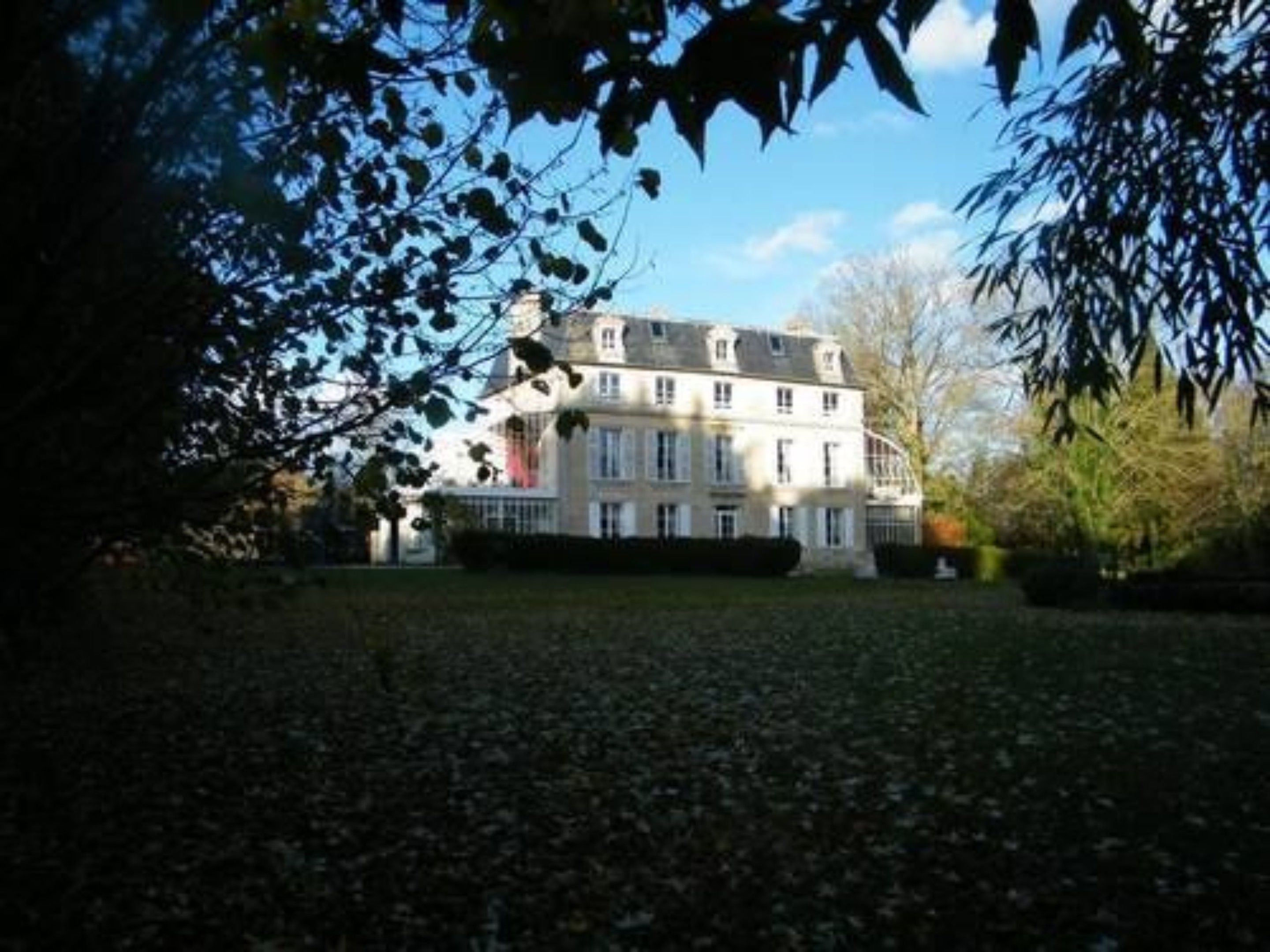 Un grand bâtiment à étages, doté d’une façade symétrique, entouré d’une pelouse bien entretenue et d’arbres matures.