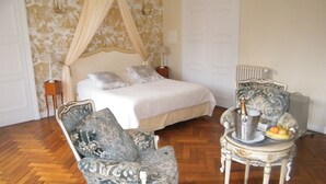 Une chambre à coucher avec un lit à baldaquin, une chaise longue, une petite table avec des fruits et un radiateur.