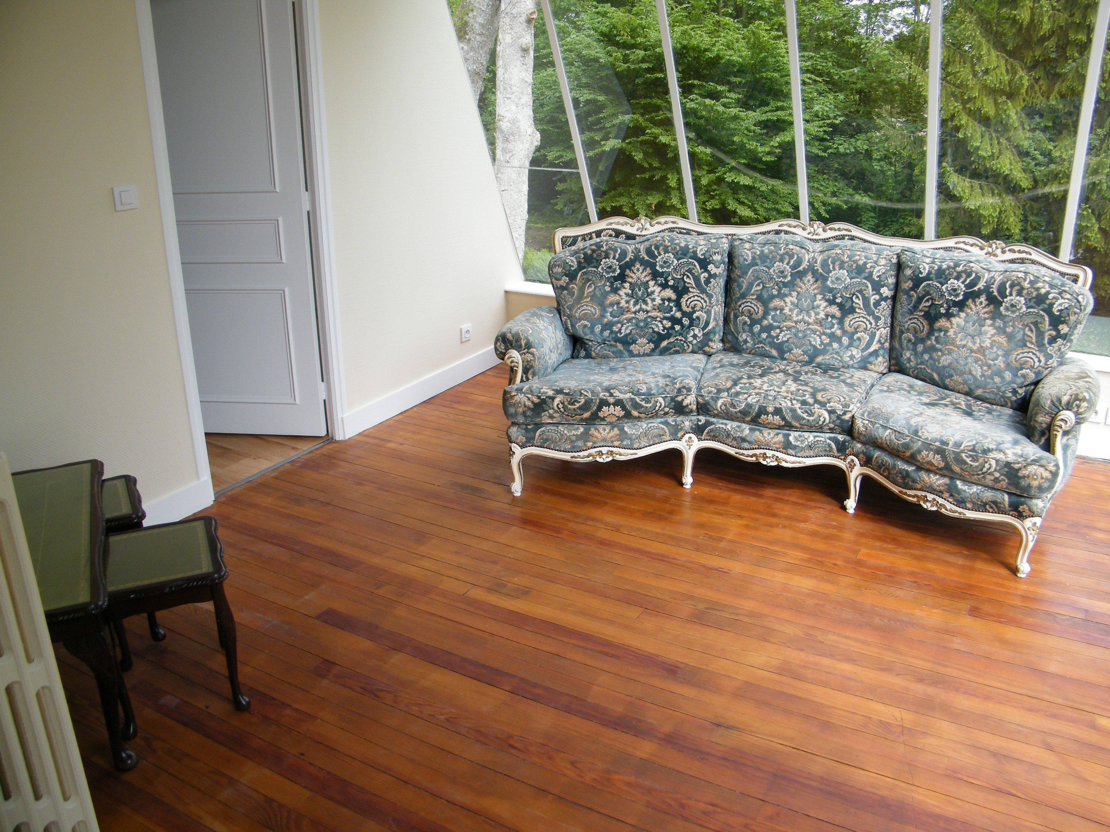 Una habitación con piso de madera, un sofá azul con estampado y una mesa de vidrio.