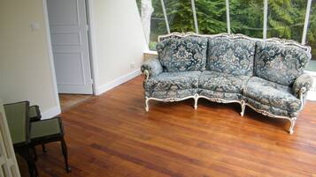 Una habitación con piso de madera, un sofá azul con estampado y una mesa de vidrio.