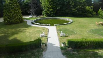 A circular garden with a central pond, surrounded by neatly trimmed hedges and statues.