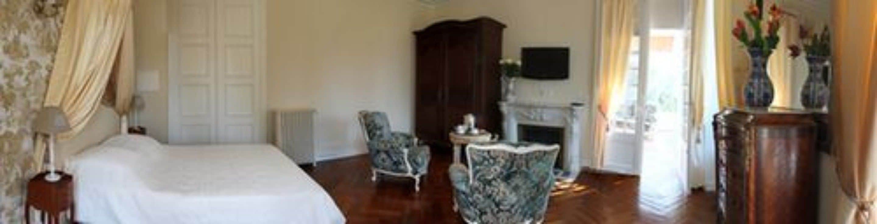 Un dormitorio con cama, dos sillas, un armario de madera, una chimenea y un televisor en la pared.