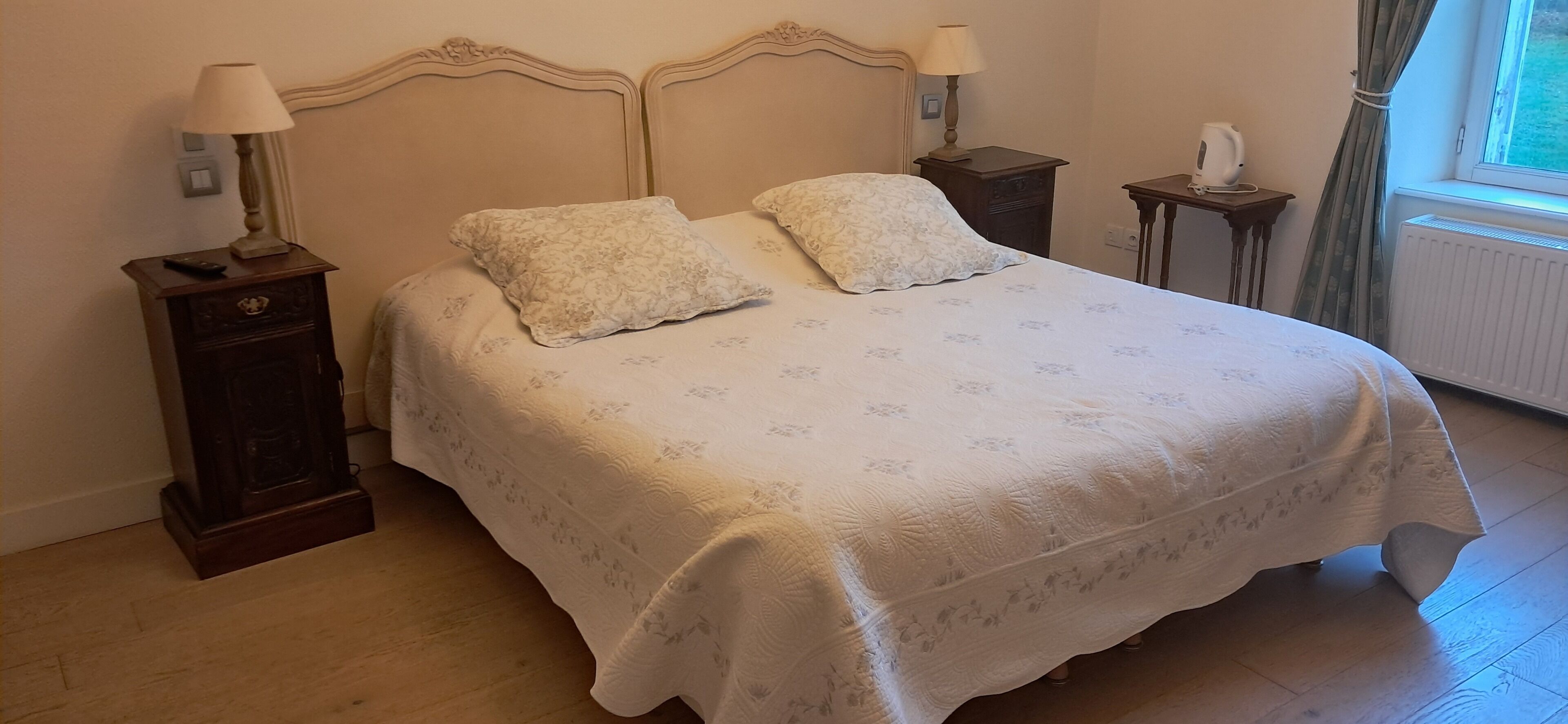 Una cama bien hecha con una colcha estampada, dos mesitas de noche con lámparas y una ventana con cortinas.