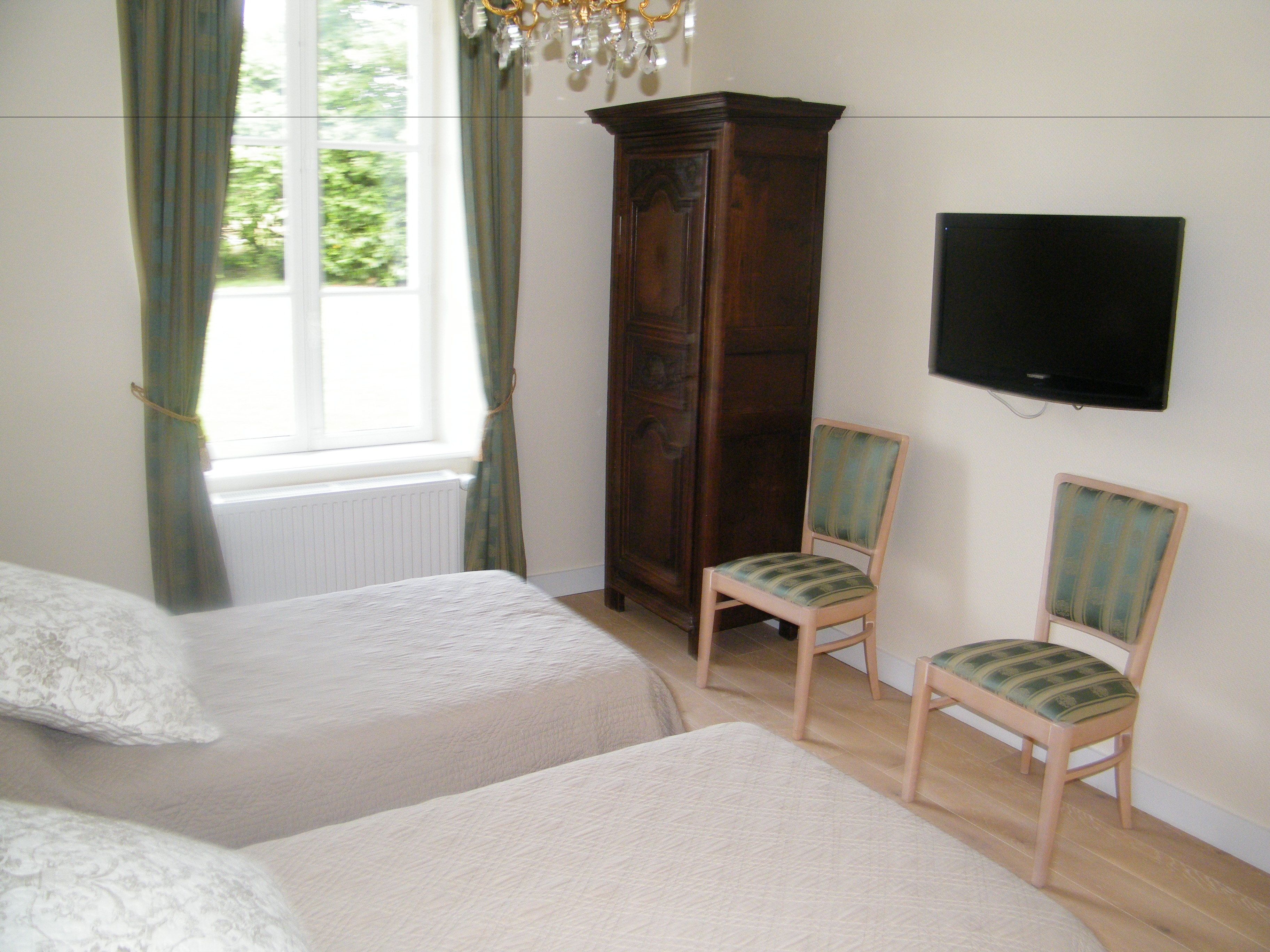 A bedroom with two beds, a wooden wardrobe, a television on the wall, and a window with curtains.