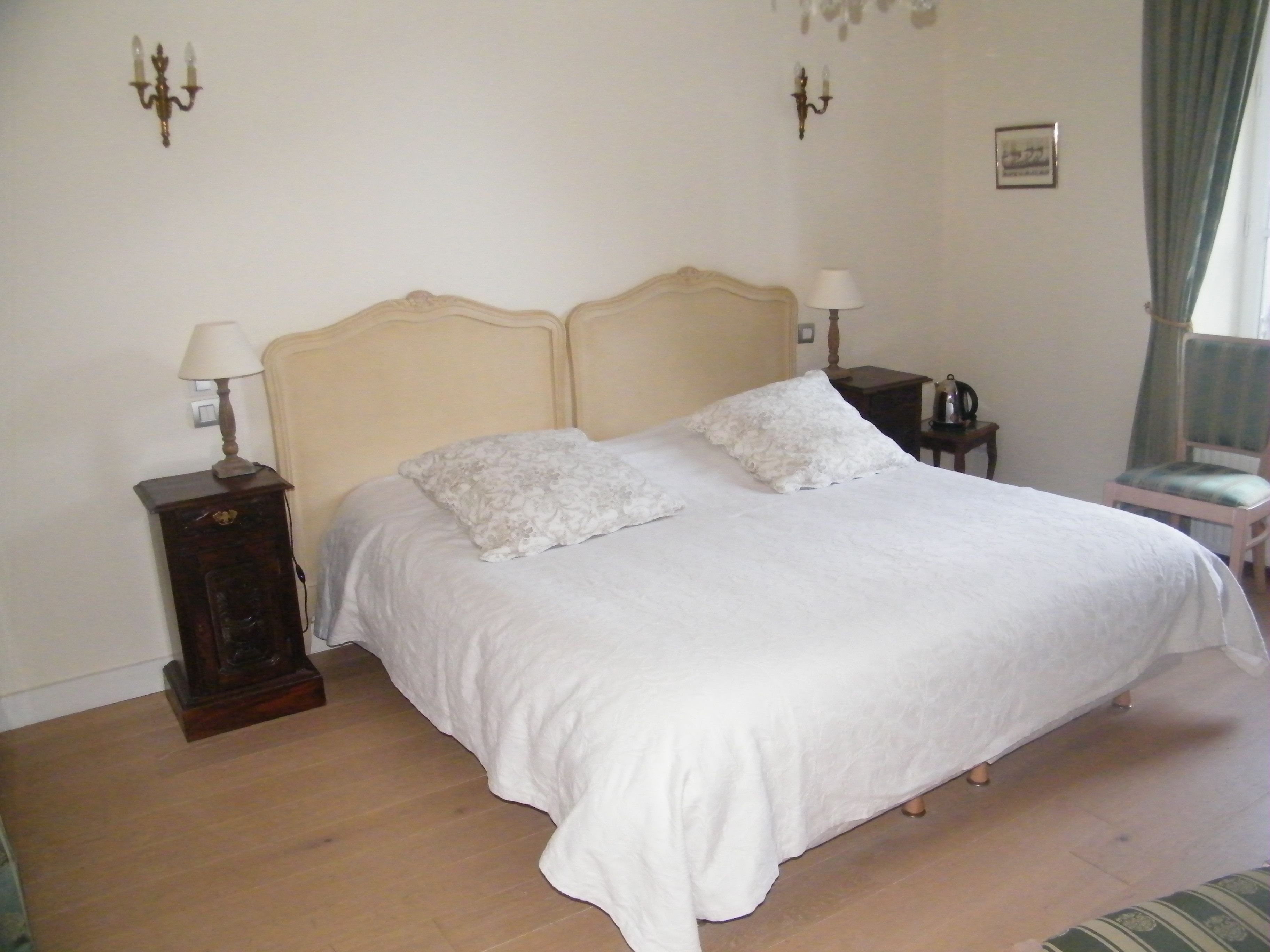 Een slaapkamer met een groot bed, twee nachtkastjes, een bijzettafeltje, een stoel en een lamp.