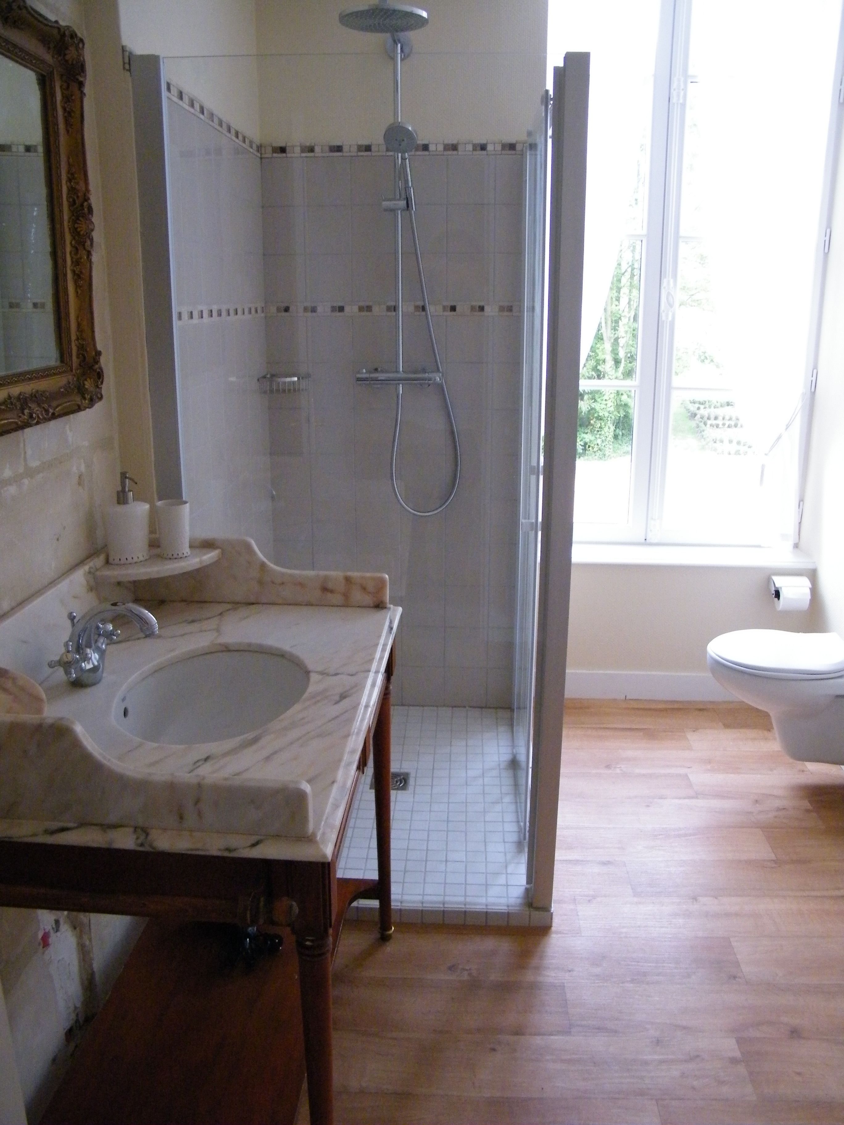 Un bagno con lavabo in marmo, mobile contenitore in legno, doccia con porta in vetro e water.