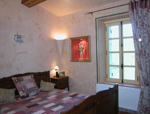 Un dormitorio con una cama de madera, una mesita de noche, un cuadro enmarcado y una ventana con cortinas.