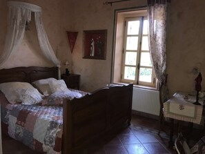 Un dormitorio con una cama de madera, una mesita de noche, una ventana con cortinas y un radiador.