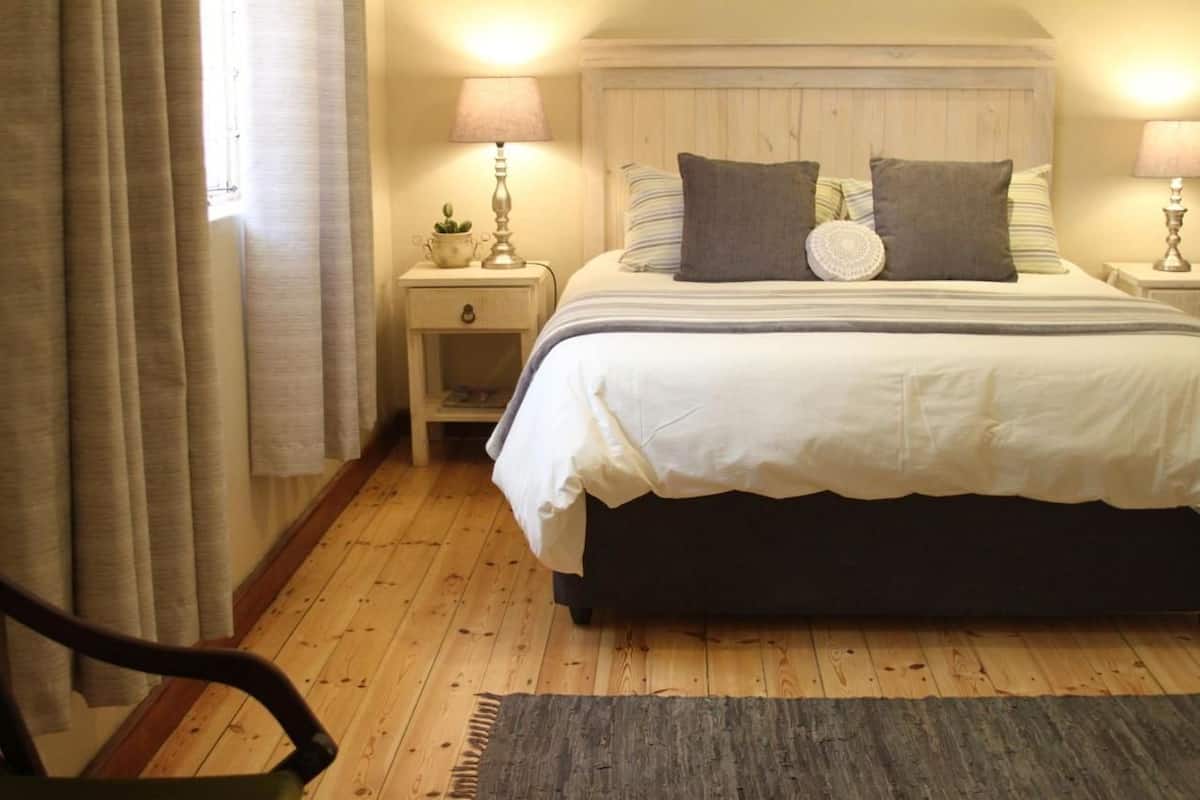 A bedroom with a large bed, two bedside tables with lamps, a small bedside table with a plant, and a chair.