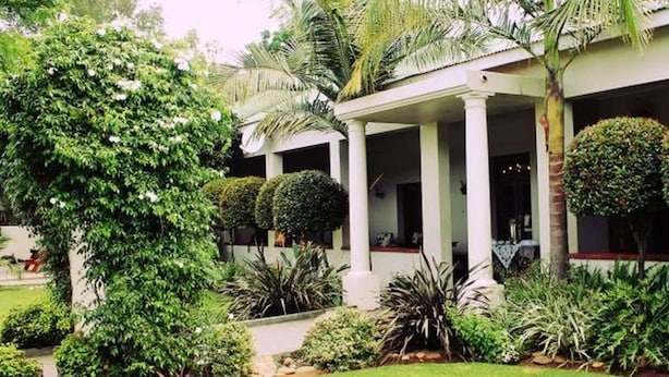 A building with a covered patio area, surrounded by well-maintained greenery and palm trees. - Ripple Hill Hotel (Patensie)
