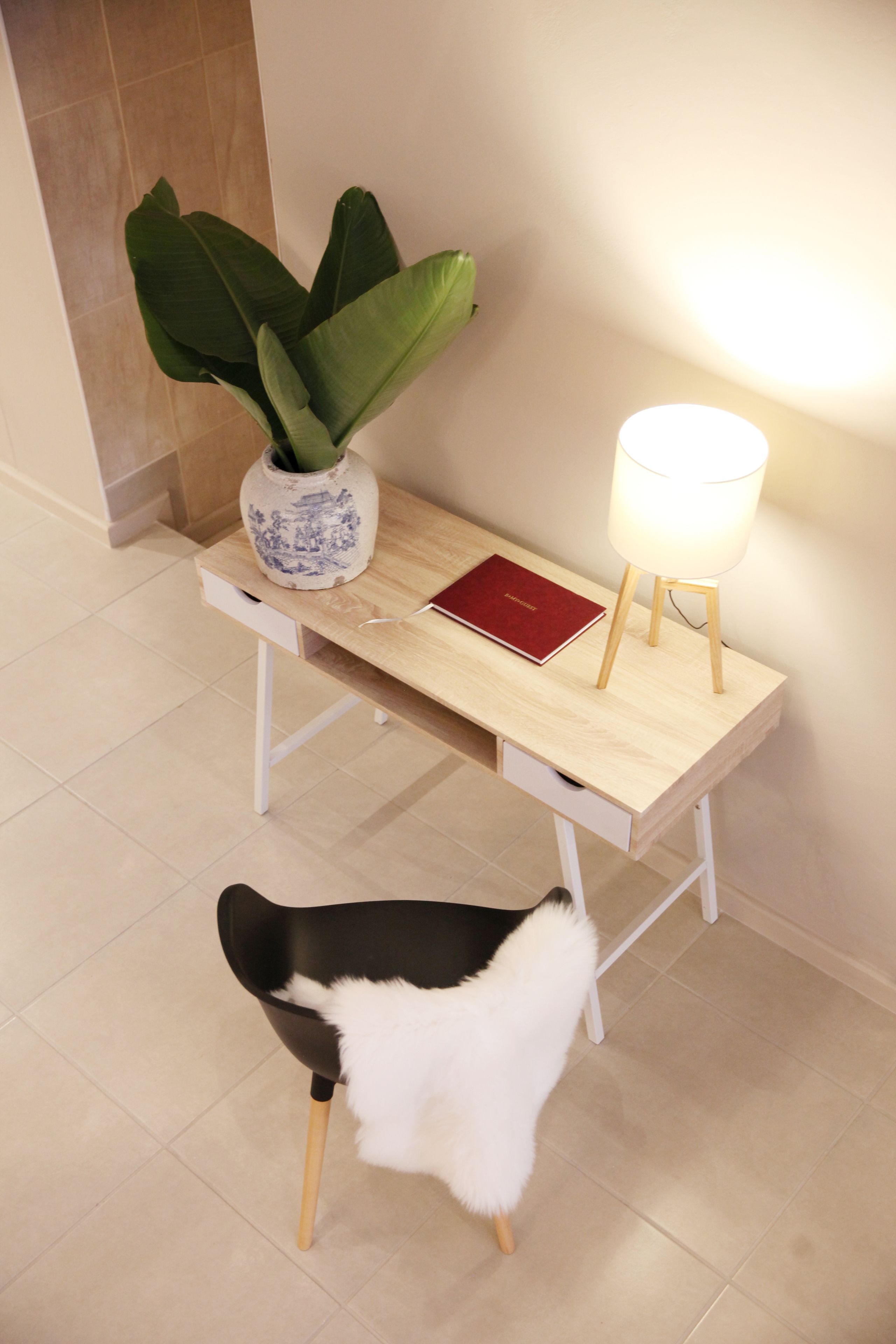 A wooden desk with a vase, a red book, and a lamp.