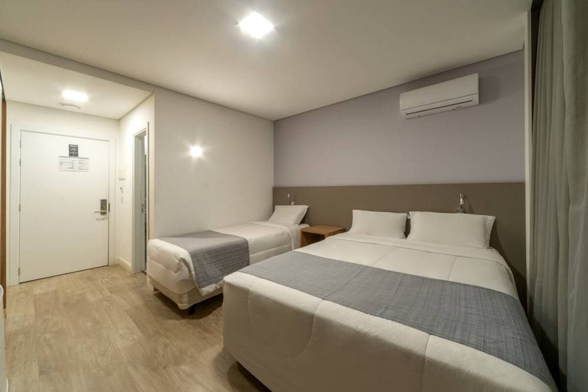 A hotel room with two beds, a wooden floor, a white door, and an air conditioning unit on the wall.