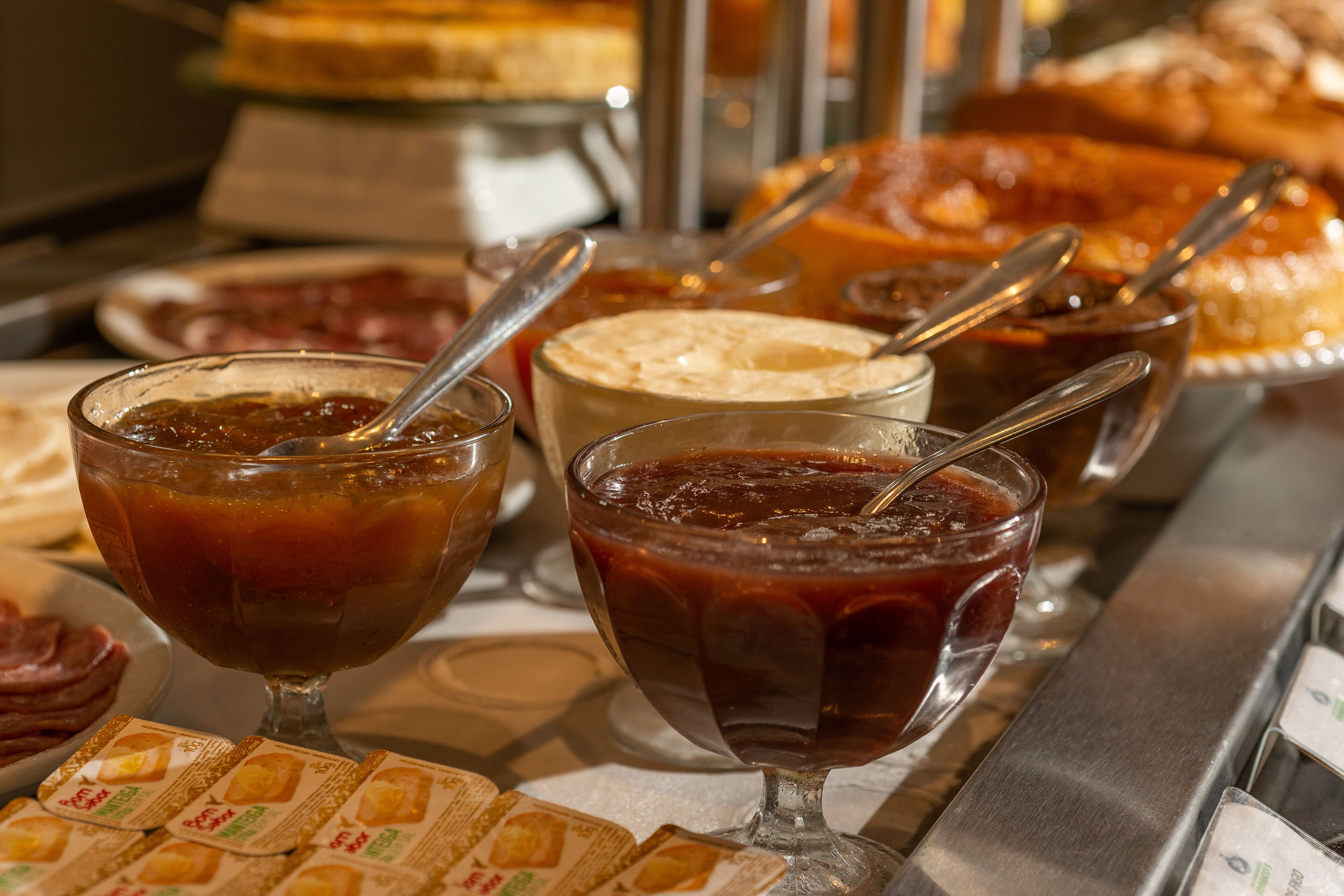 Un bufé con diversos alimentos y bebidas, incluyendo una selección de mermeladas y un pastel.
