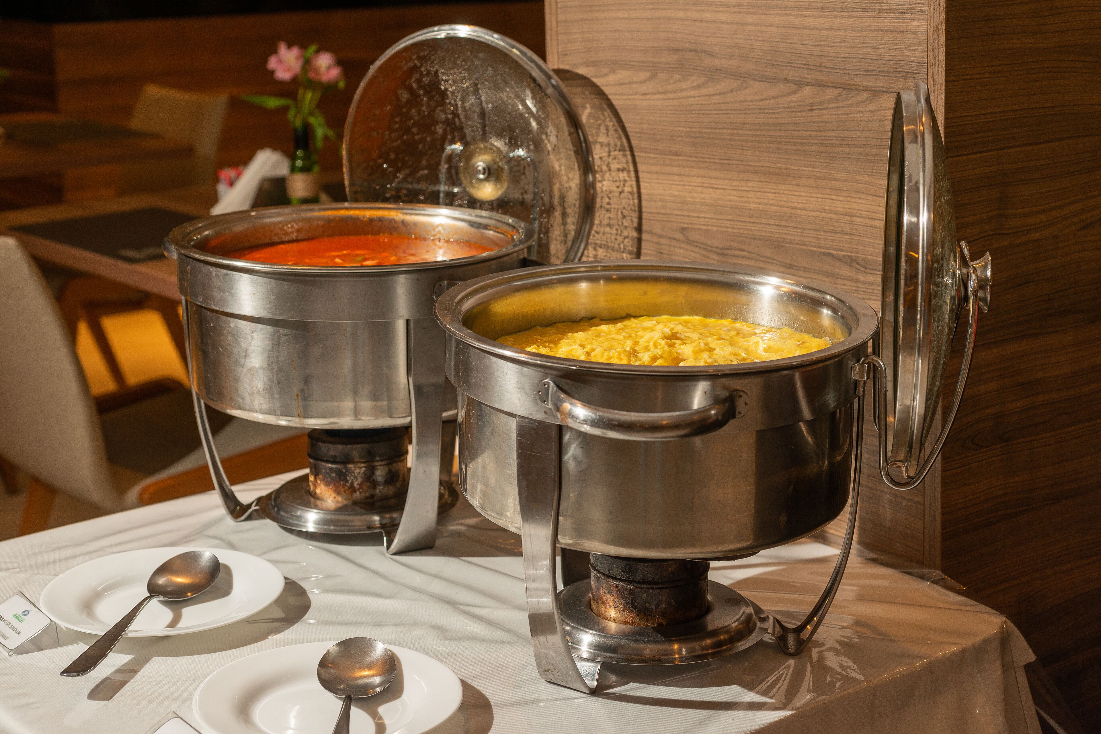 Twee roestvrijstalen chafing dishes met deksels op een tafel, samen met witte borden en lepels.