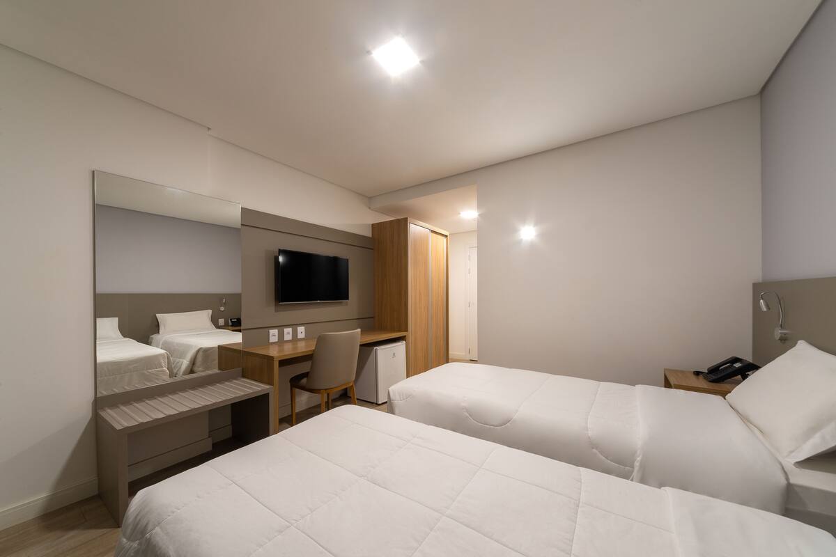 A modern hotel room with two beds, a desk, a chair, a TV, and a wardrobe.