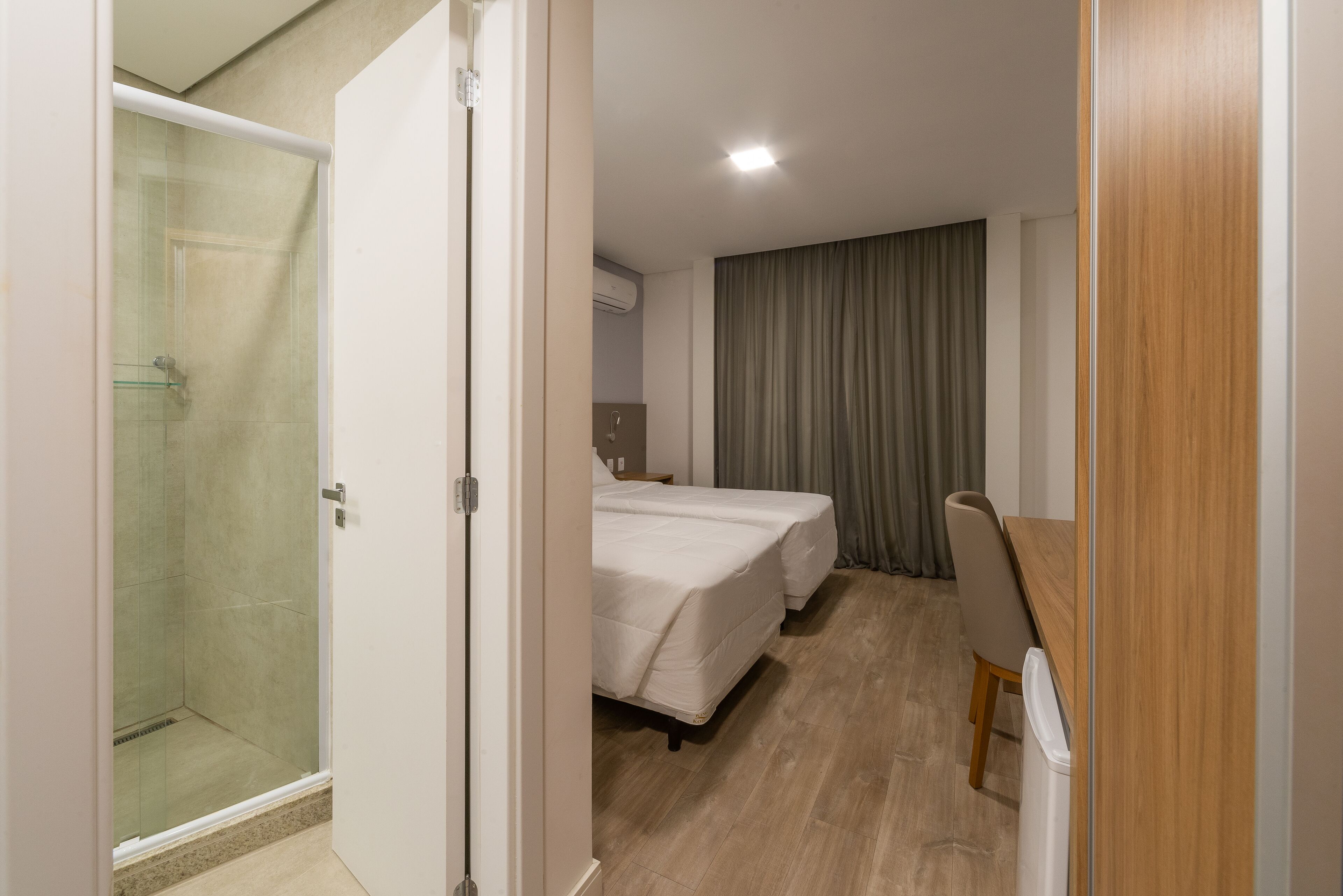 Quarto de hotel com chuveiro, duas camas, escrivaninha e uma cadeira.