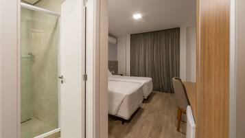 Quarto de hotel com chuveiro, duas camas, escrivaninha e uma cadeira.