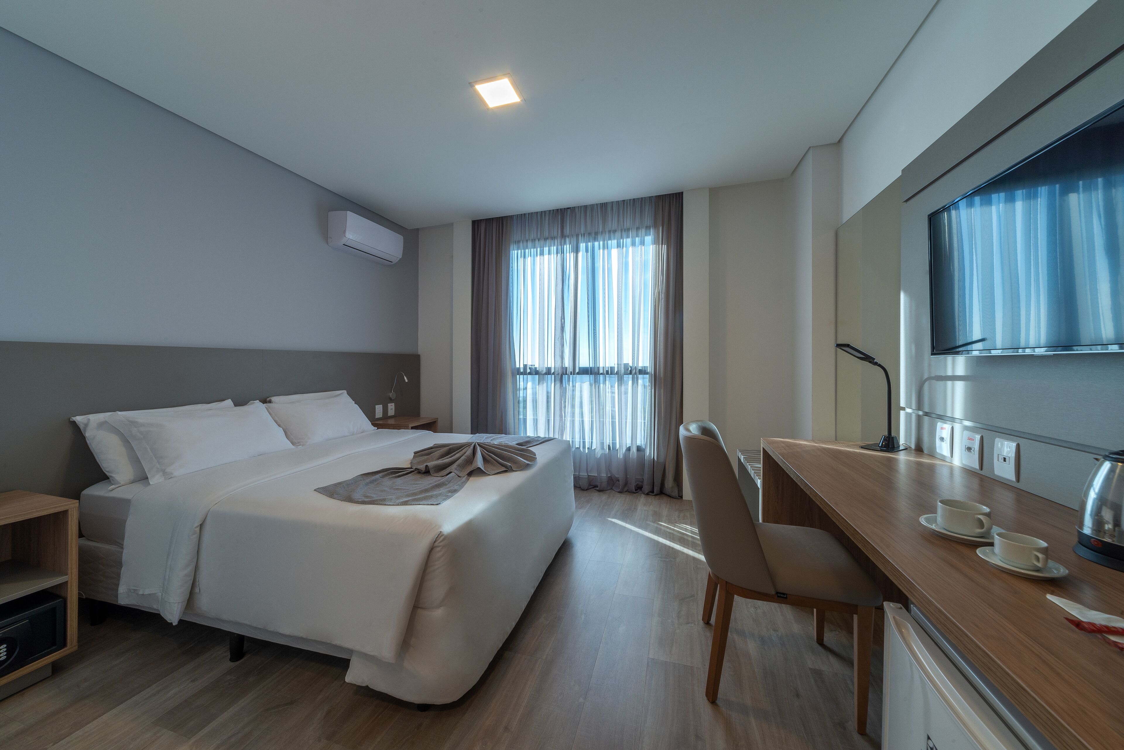 A modern hotel room with a large bed, a desk, and a television.