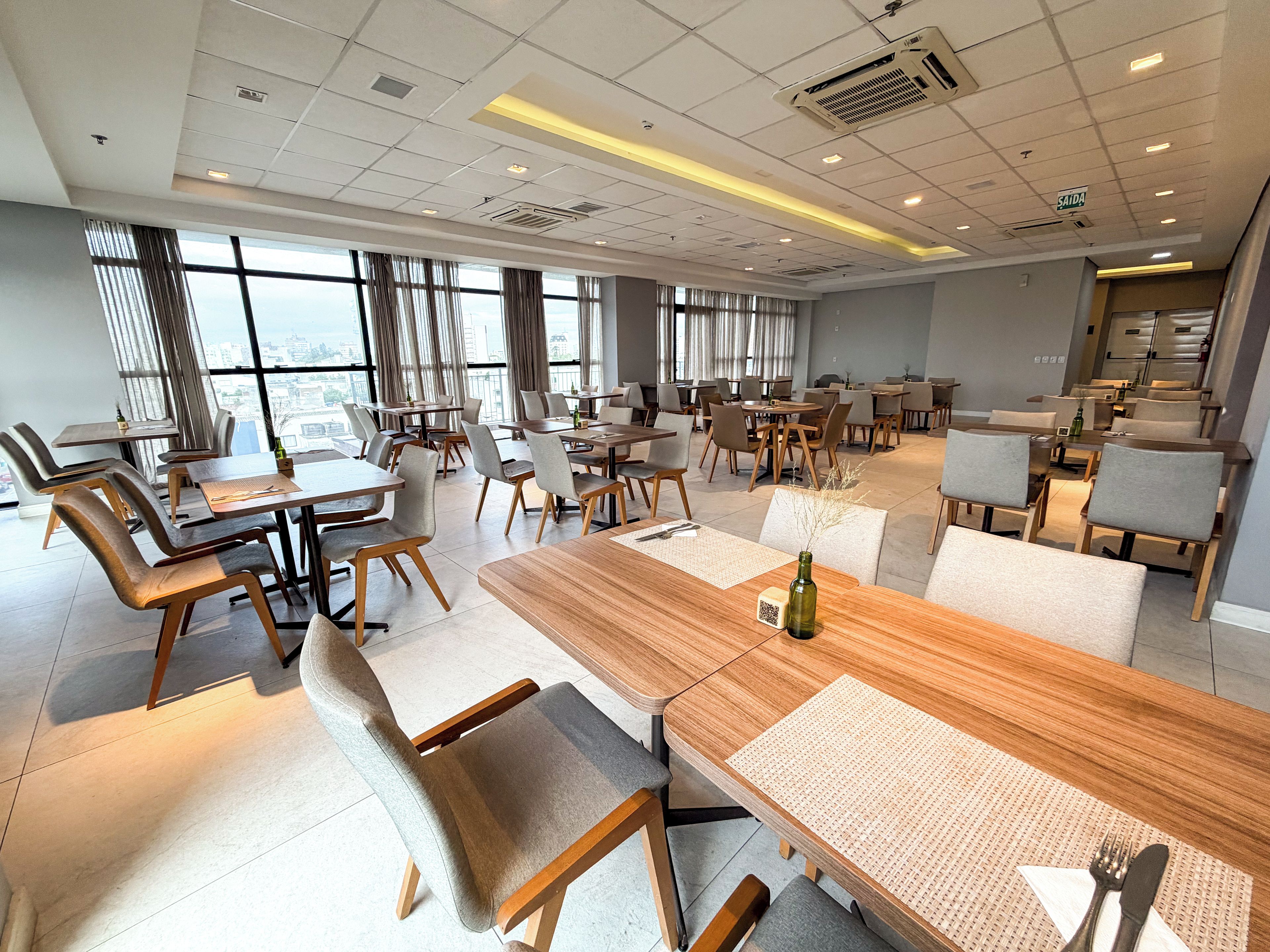 Un'ampia sala da pranzo con diversi tavoli e sedie, grandi finestre e un moderno design del soffitto.