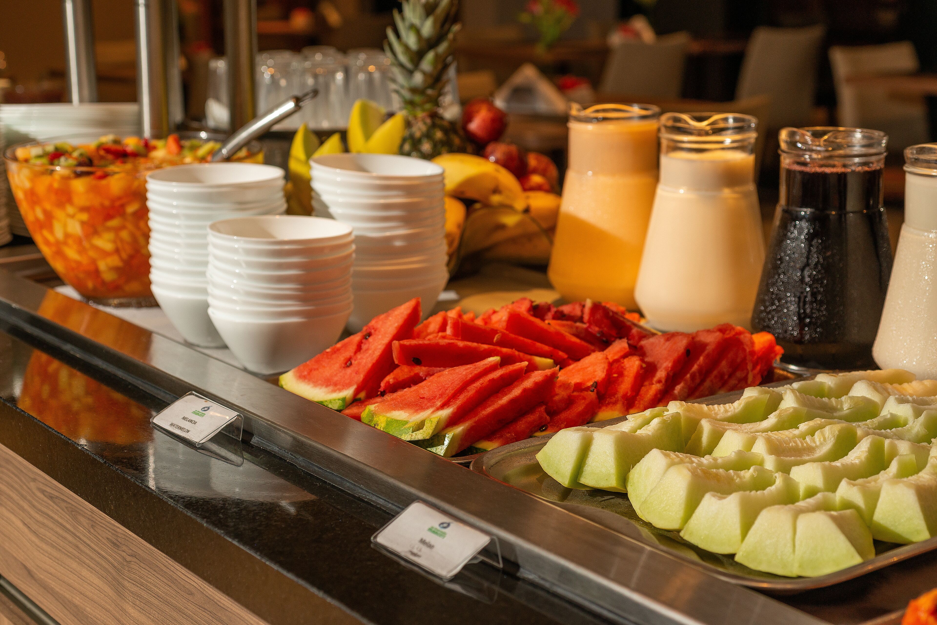 Un bufé con diversas frutas, como sandía y melón, y varias opciones de bebidas.