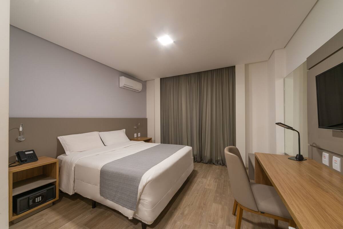 A hotel room with a bed, bedside table, desk, chair, and a television.
