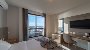 A modern hotel room with a large bed, a desk, a chair, a TV, and a view of the city. -  Laghetto Rio Grande (Rio Grande)
