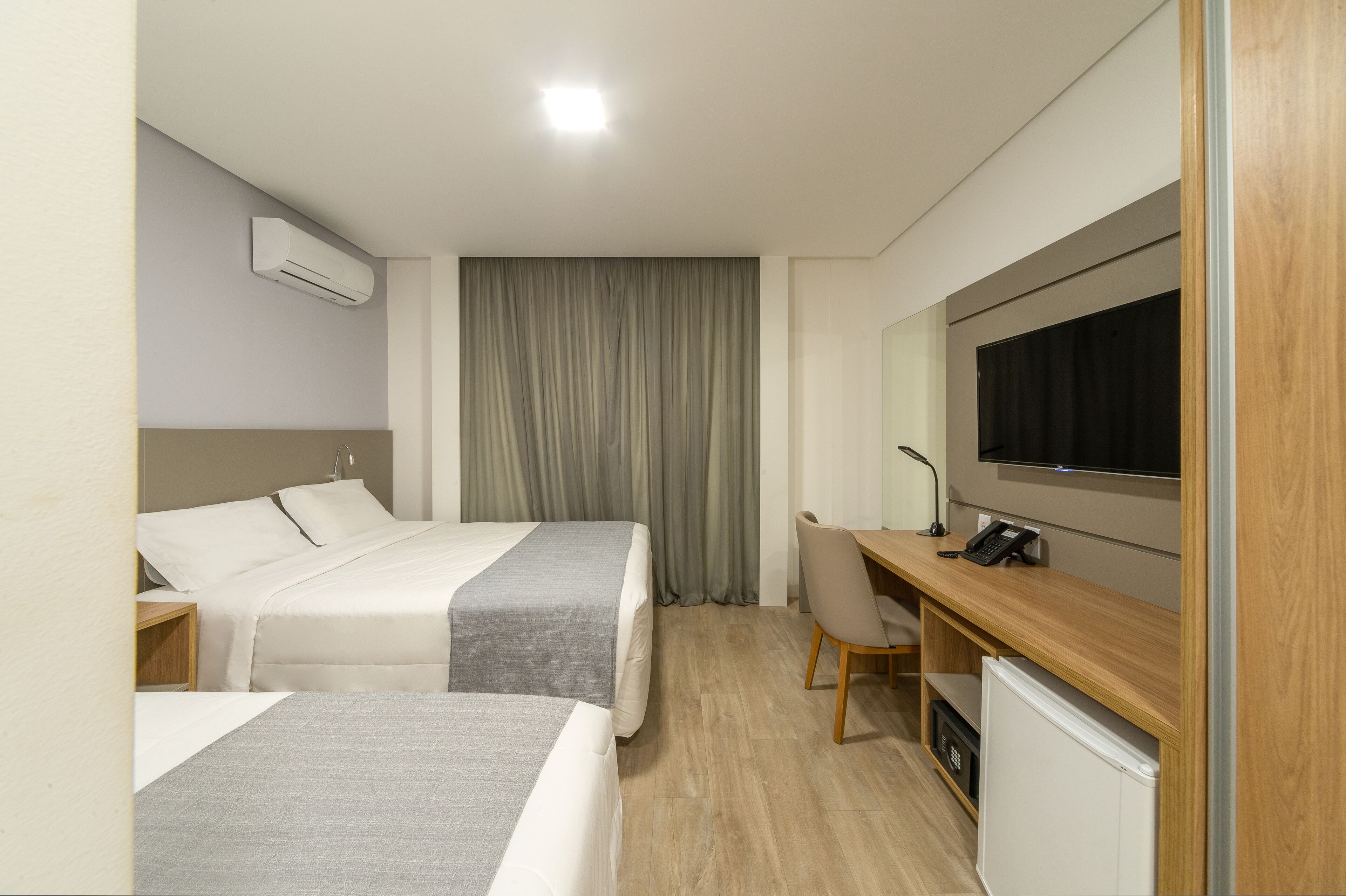 Ein Hotelzimmer mit zwei Betten, einem Schreibtisch mit Stuhl, einem Fernseher und einer Klimaanlage.