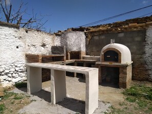 An outdoor kitchen area with a stone wall, a brick oven, and a concrete table.