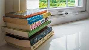 A stack of books on a windowsill with a view of a green landscape through a window. - The Kestrel B&B (Crickhowell)