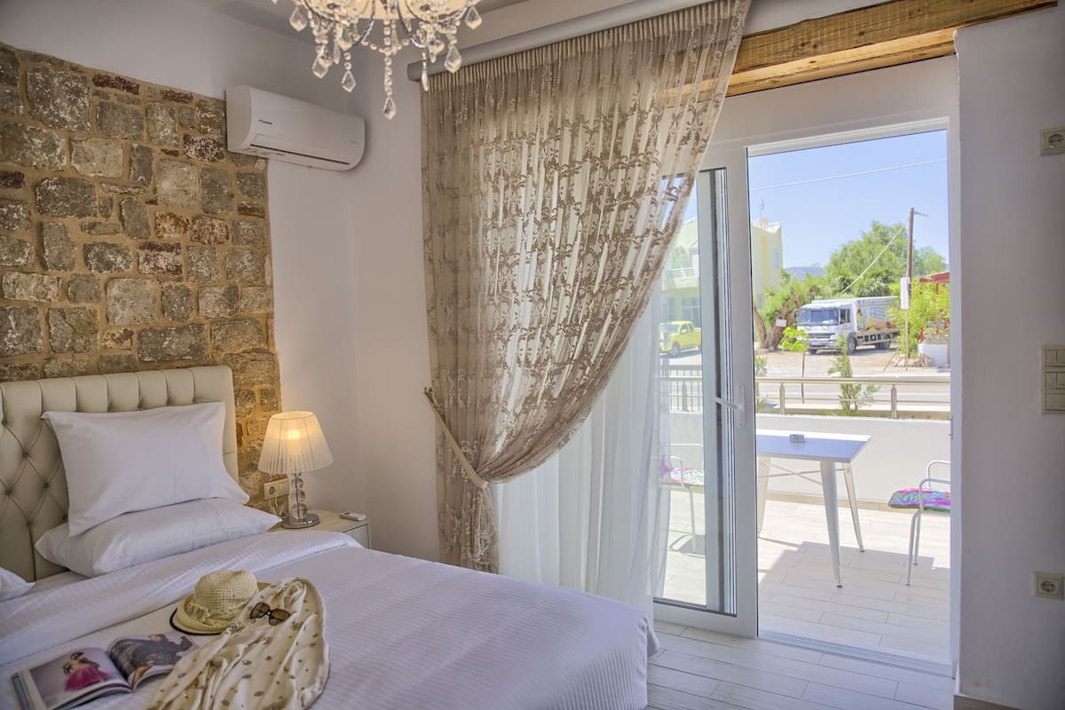 A bedroom with a stone wall, a bed with white linens, a bedside lamp, and a view of the outside.