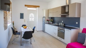 A compact kitchen with a dining area, a built-in oven, and a TV mounted on the wall. - G&K Stone Suites (Rhodes)