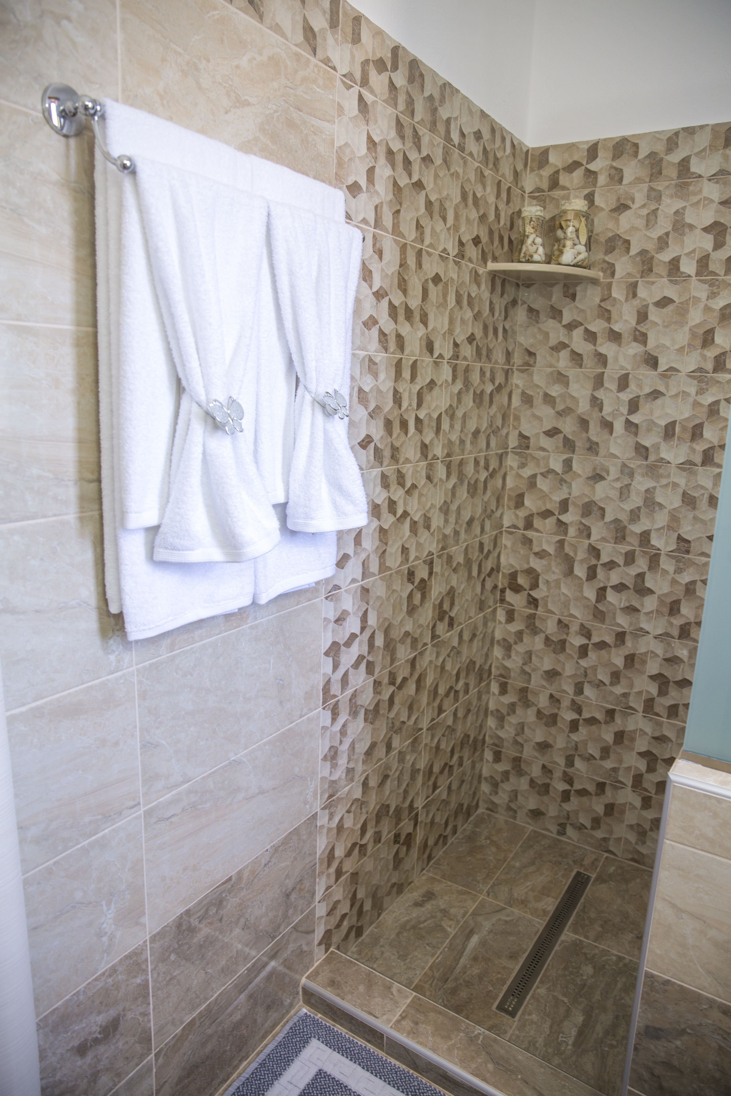 Un espace douche avec un mur texturé, un porte-serviettes avec deux serviettes et une étagère avec des objets décoratifs.