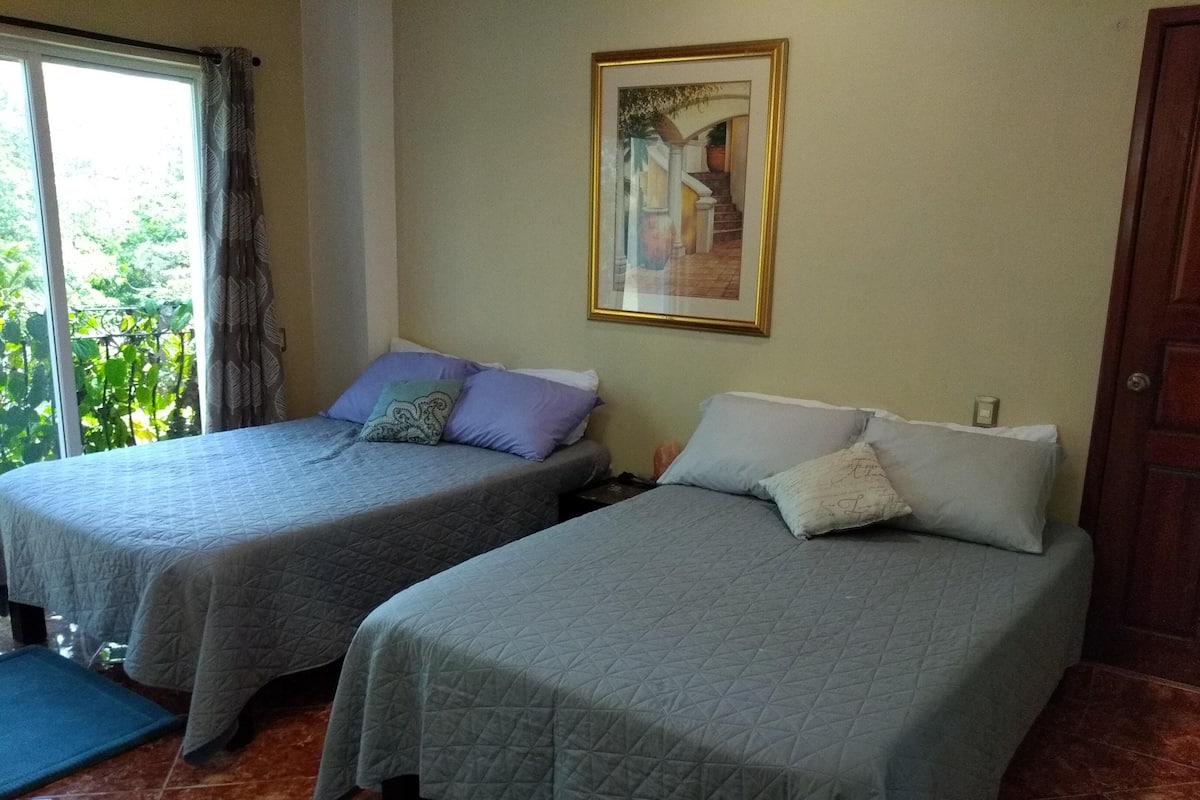 Two single beds with grey quilts, a framed picture on the wall, and a door to the right.