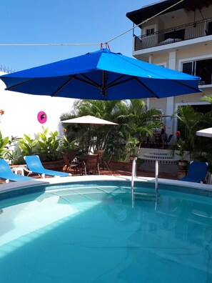 Zona de piscina amb gandules blaves, una taula i ombrel·les.