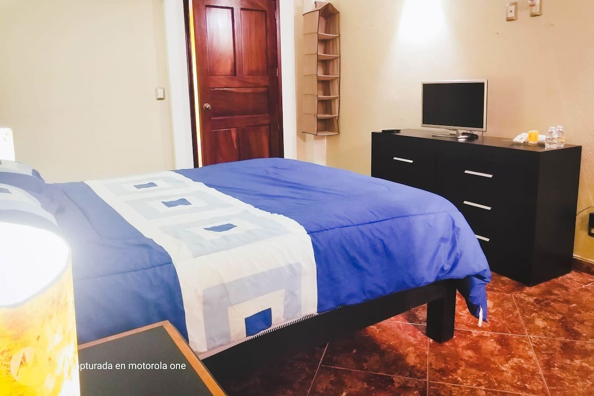 A bedroom with a bed, a TV, a dresser, and a door.