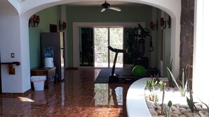 Amplia sala de estar con un ventanal grande, ventilador de techo y una caminadora.