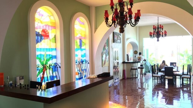 Un vestíbulo de hotel con un mostrador de recepción, ventanales arqueados con vidrieras de colores y una araña.